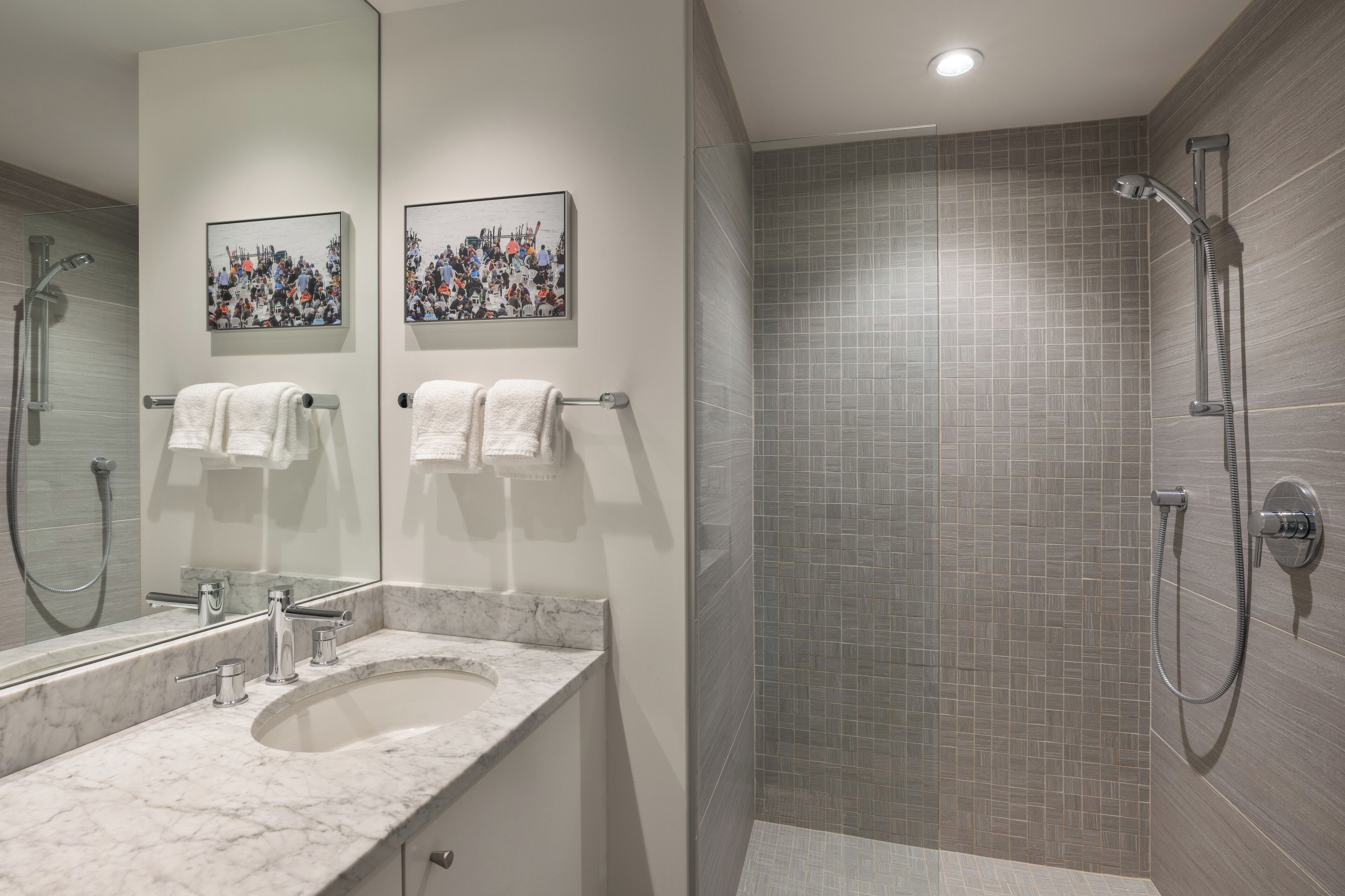 A modern bathroom with a marble sink, two framed pictures on the wall, and a shower with grey tiles.