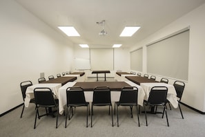 A conference room with a long table, chairs, a projector, and a screen. - Hotel San Alberto (Hermosillo)