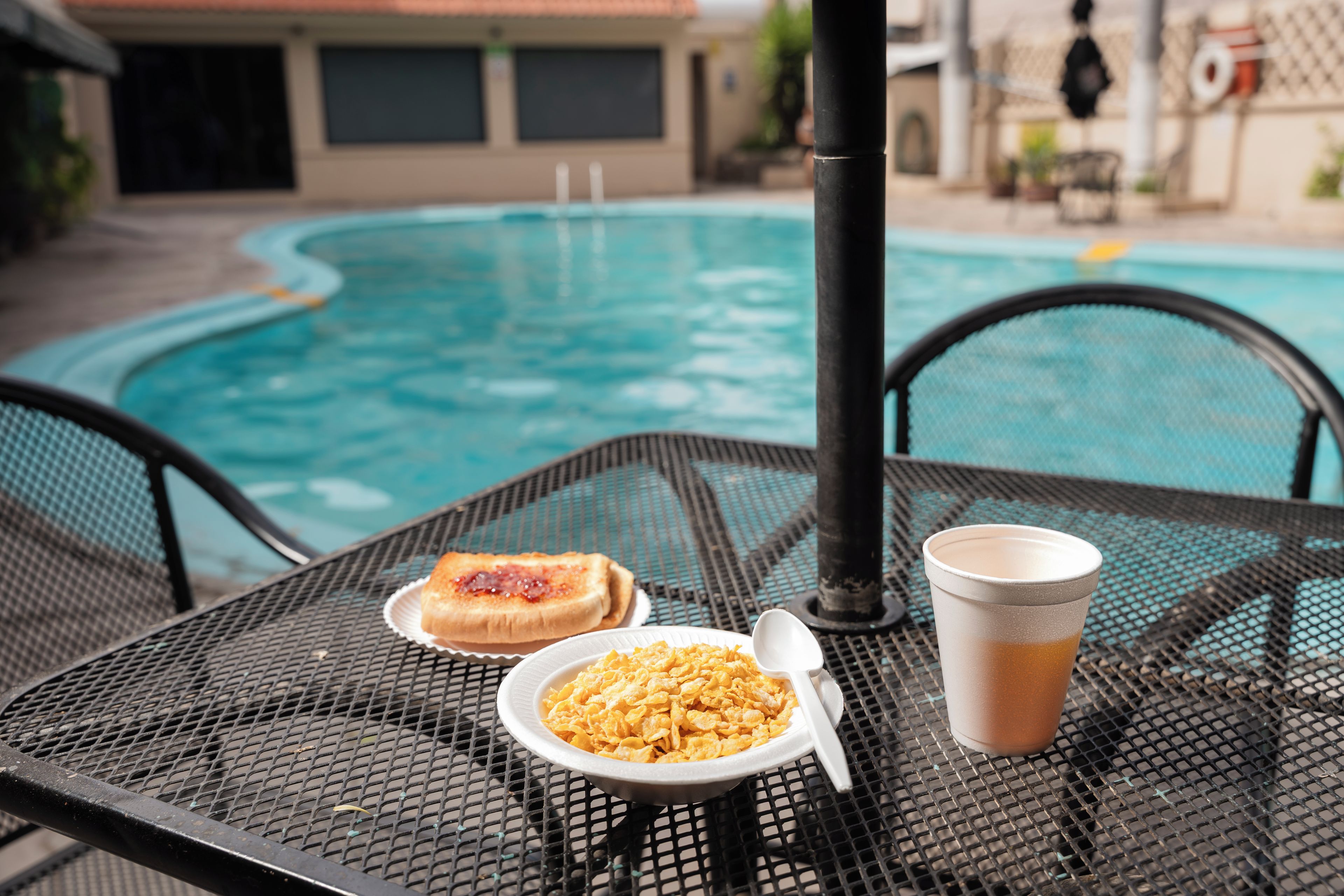 Una mesa con alimentos para el desayuno y una bebida cerca de una piscina.