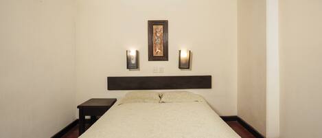 A hotel room with a bed, a nightstand, two wall-mounted lights, and a framed picture above the bed.