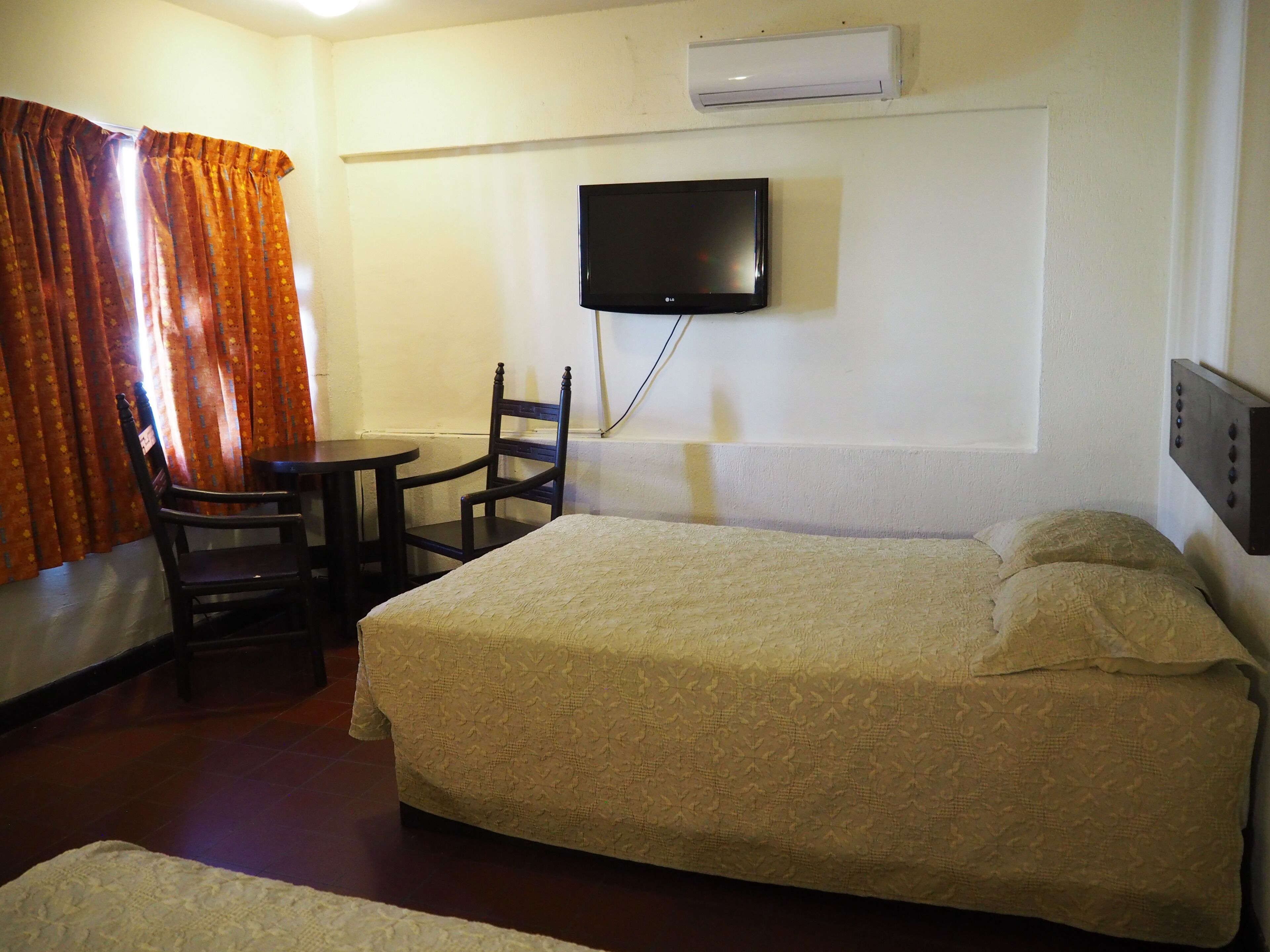 Una camera d'albergo con un letto, una sedia, un tavolino, una televisione e un condizionatore d'aria.
