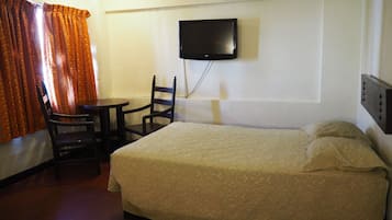 Una camera d'albergo con un letto, una sedia, un tavolino, una televisione e un condizionatore d'aria.