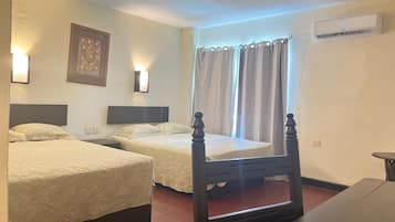 Habitación de hotel con dos camas, cabecero de madera, mesita de noche, aire acondicionado instalado en la pared y una ventana con cortinas.