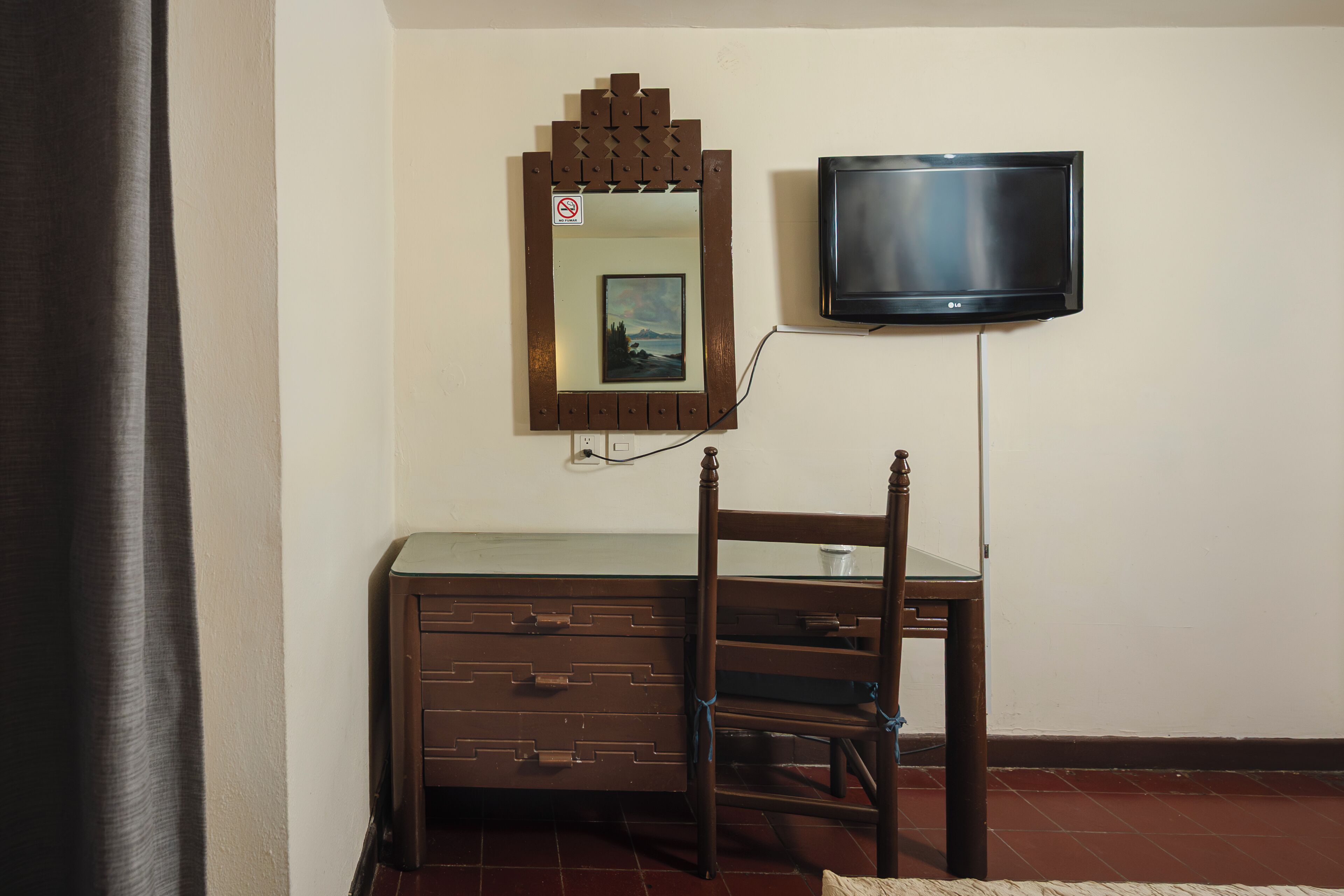 Una habitación con un aparador de madera, una silla, un televisor montado en la pared y un espejo con un marco decorativo.