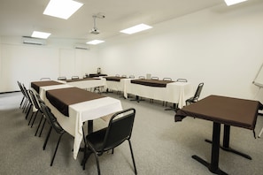 A conference room with tables and chairs, a projector, and an air conditioning unit. - Hotel San Alberto (Hermosillo)