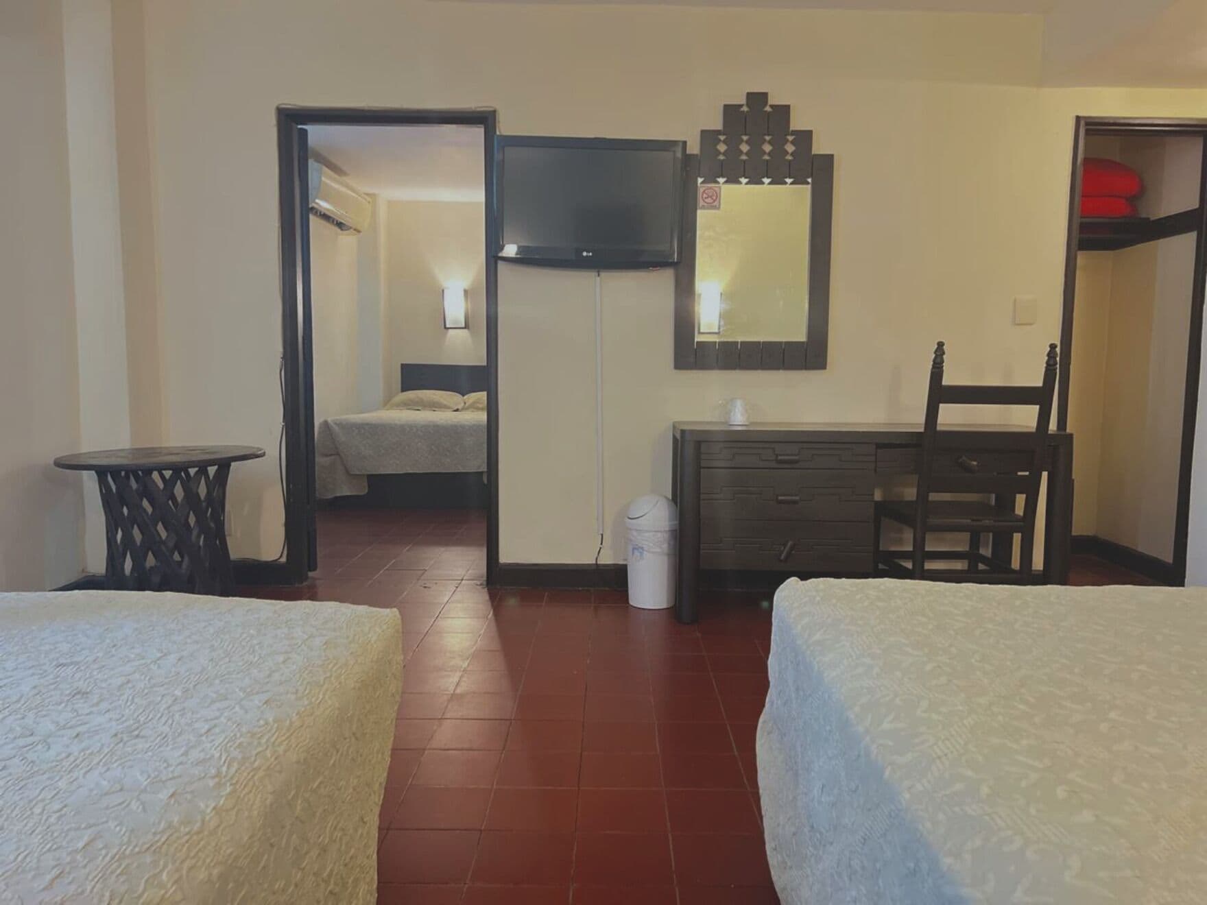 Quarto de hotel com duas camas, uma cômoda, uma cadeira, uma televisão e um espelho.