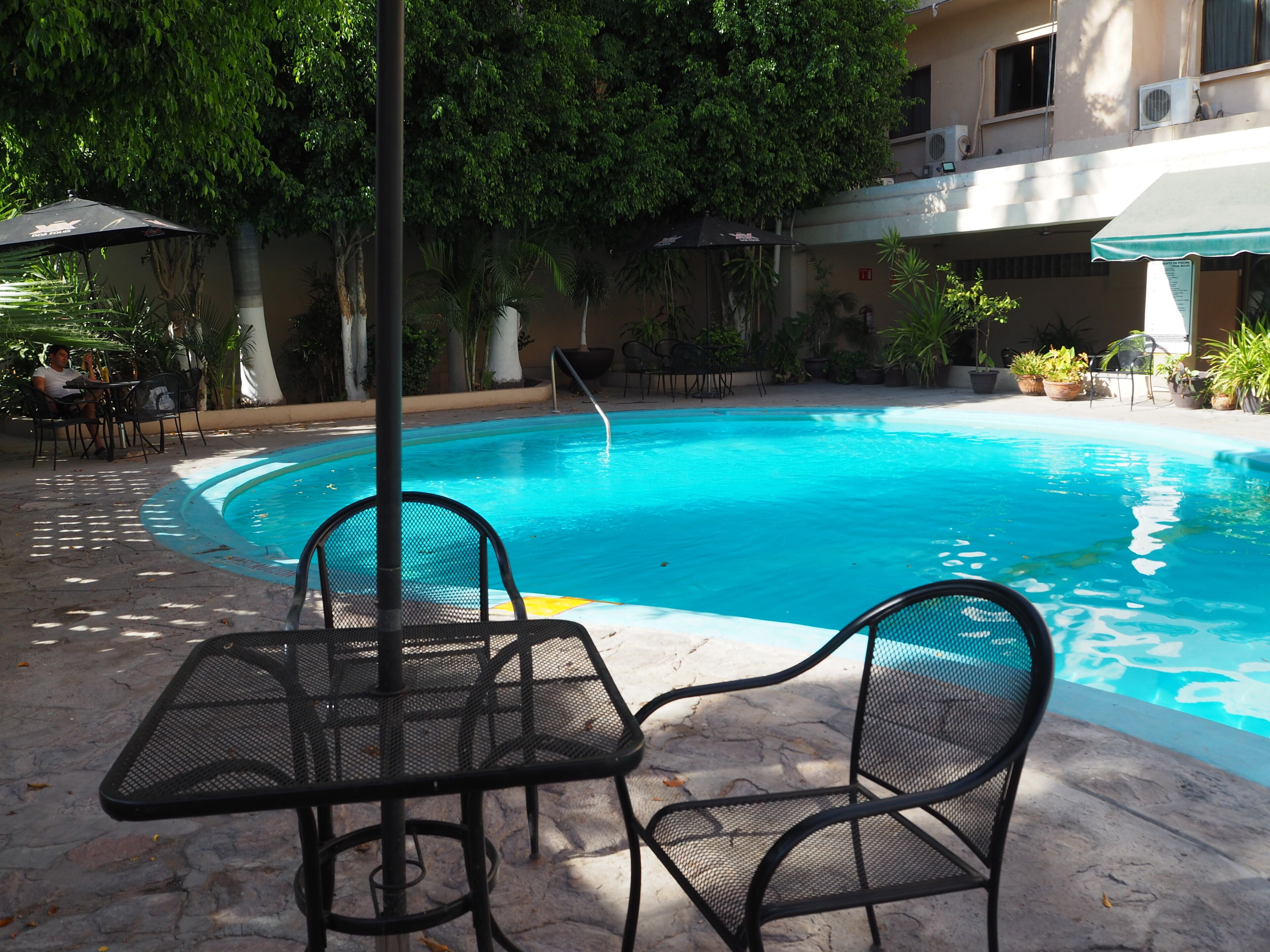 Una piscina con borde de azulejos, rodeada de mobiliario exterior y plantas en macetas.
