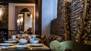 A dining area with a brick wall, ornate gold detailing, and a long table set for a meal. - Antica Locanda (Rome)