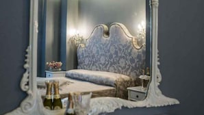 A bedroom with a large ornate mirror, a bed with a patterned headboard, and a bedside table with a tray of champagne bottles and glasses. - Antica Locanda (Rome)