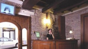 A reception desk with a wooden finish, a stone wall, and a car visible through the door. - Antica Locanda (Rome)