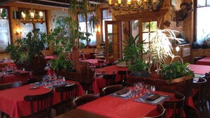 A restaurant with wooden interiors, red tablecloths, and hanging plants. - Hotel Les Touristes (Abondance)