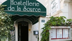 Ingången till Hostellerie de la Source kännetecknas av ett grönt solskydd, en skylt med menyer och siffran 7 på byggnaden.