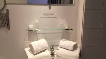 A bathroom with a white sink, two towels, a glass shelf with toiletries, and a mirror.