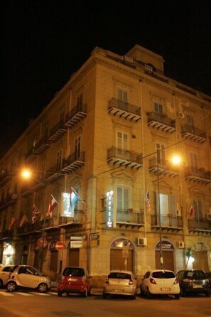 A multi-story building with balconies, parked cars, and flags. - Hotel Florio (Palermo)