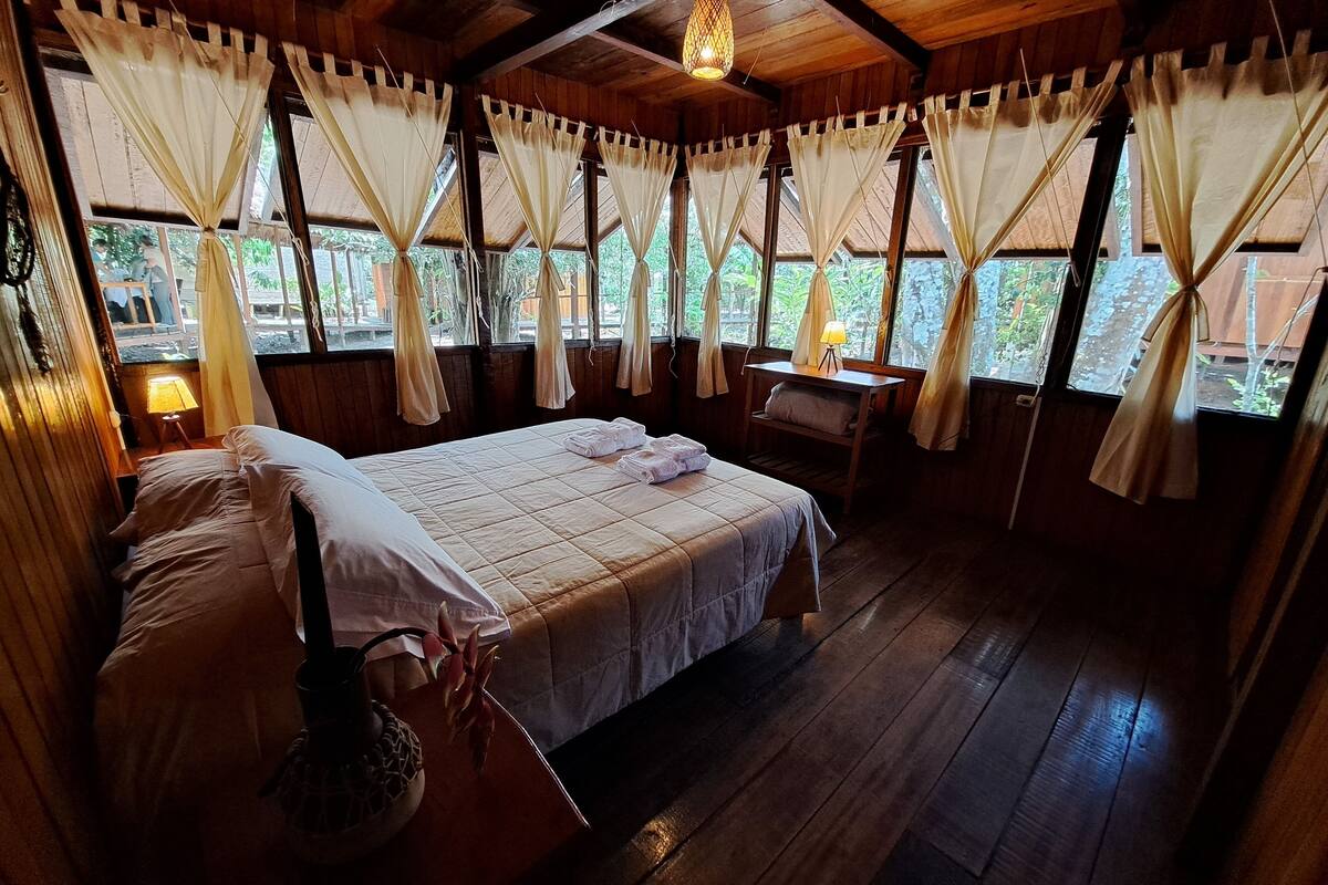A wooden room with a bed, a desk, and a window with curtains.