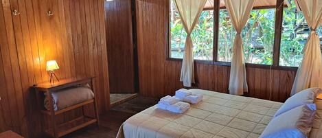 Una habitación de madera con una cama, un banco, una mesa y una lámpara.