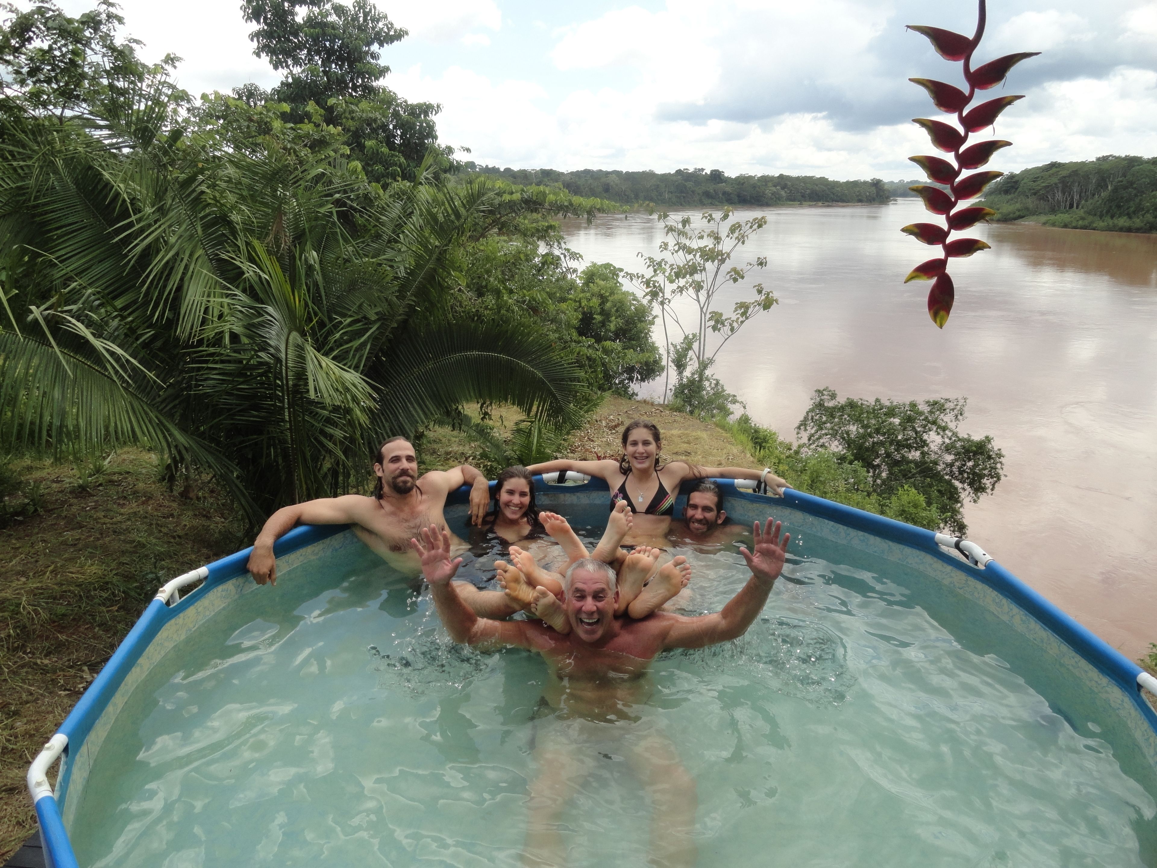 A group of people in a blue inflatable pool surrounded by lush greenery and a river.