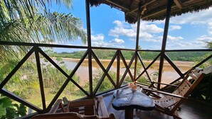 Terraza de madera con mesa y sillas con vistas a un río y follaje.
