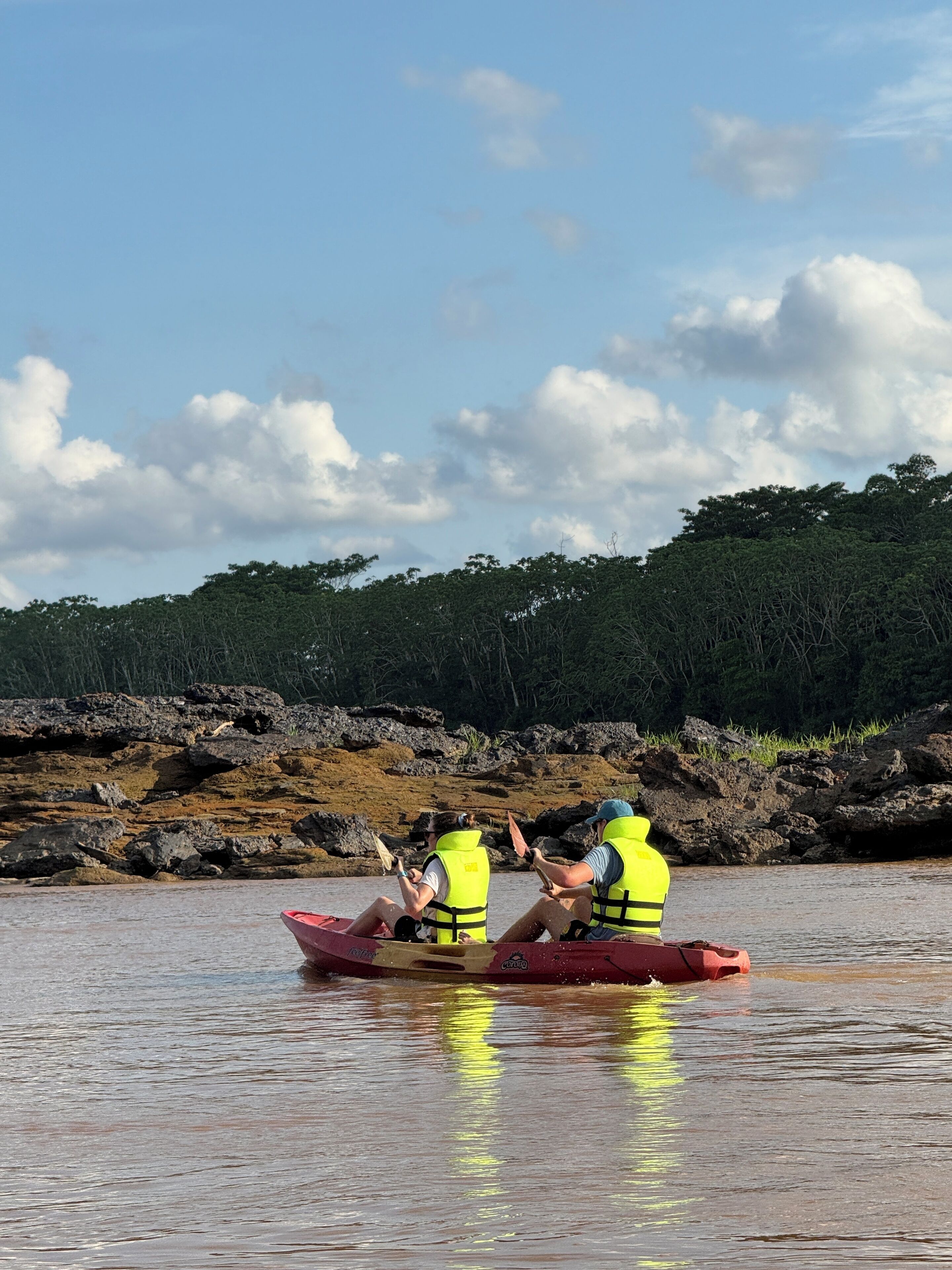 Two people in a red canoe on a calm river, wearing yellow life jackets.
