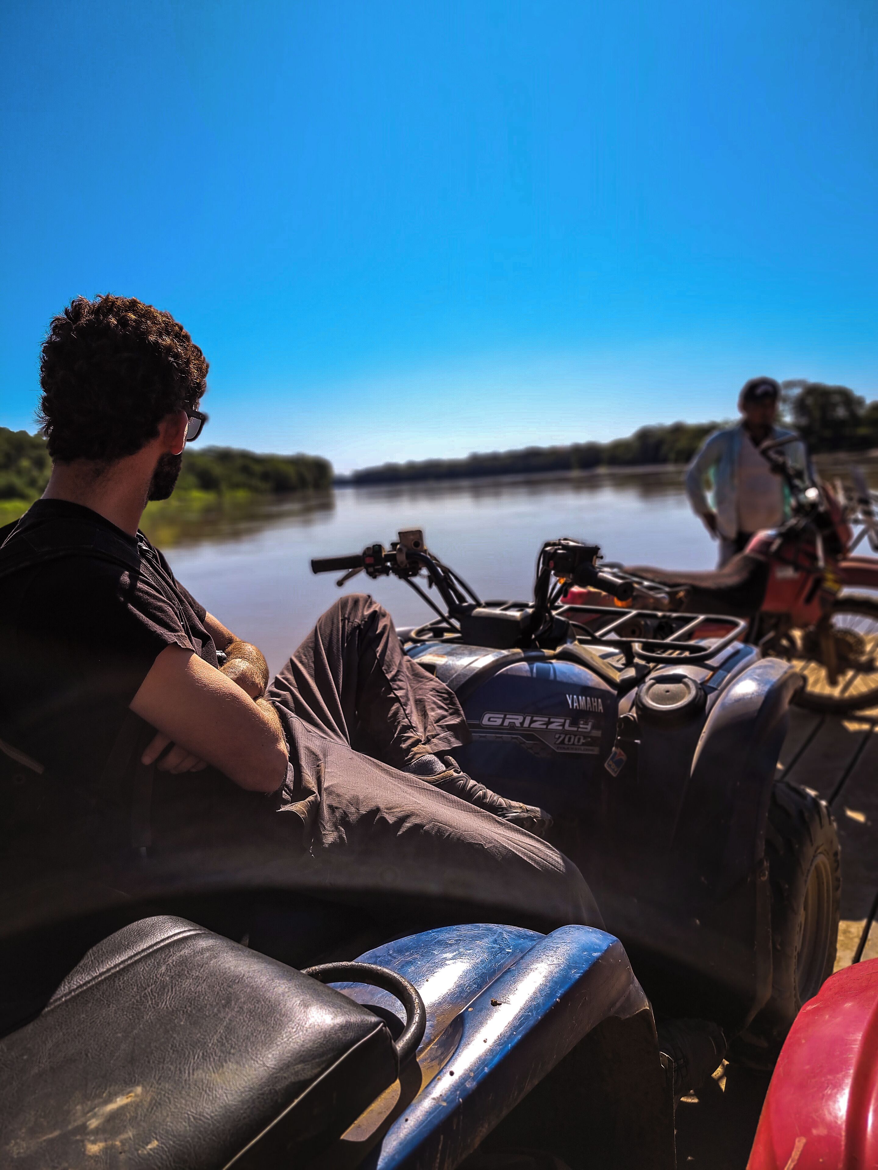 A person sitting on a boat with a Yamaha Grizzly 700 outboard motor, overlooking a calm river.