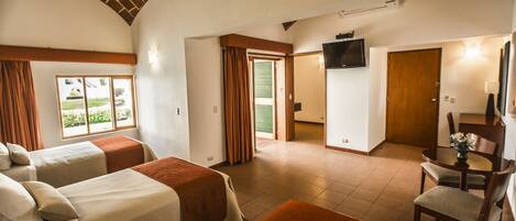A hotel room with two beds, a TV, a dining area, and a view of the outdoors.