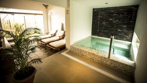 A modern indoor pool area with lounge chairs, a potted plant, and a tiled floor. - Hotel Las Dunas (Ica)