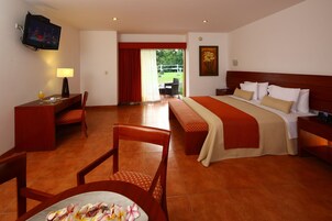 Habitación de hotel con cama, mesita de noche, televisor, escritorio con silla y vistas al exterior.