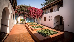 A courtyard with a central pathway, surrounded by brick planters and a building with arches and a balcony. - Hotel Las Dunas (Ica)