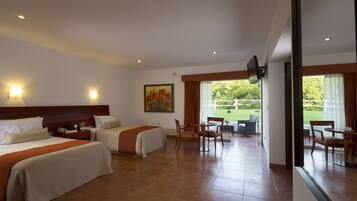 Habitación de hotel con dos camas, una mesa de comedor, sillas, un televisor y un cuadro.