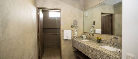 Un baño moderno con encimera de granito, dos lavamanos, un espejo grande y una zona de ducha.