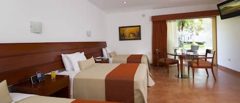 A hotel room with two beds, a dining table, chairs, a TV, and a painting on the wall.