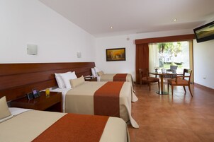 Habitación de hotel con dos camas, una mesa de comedor, sillas, un televisor y un cuadro en la pared.