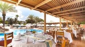 A poolside restaurant with tables set for dining, overlooking a swimming pool. - Hotel Las Dunas (Ica)