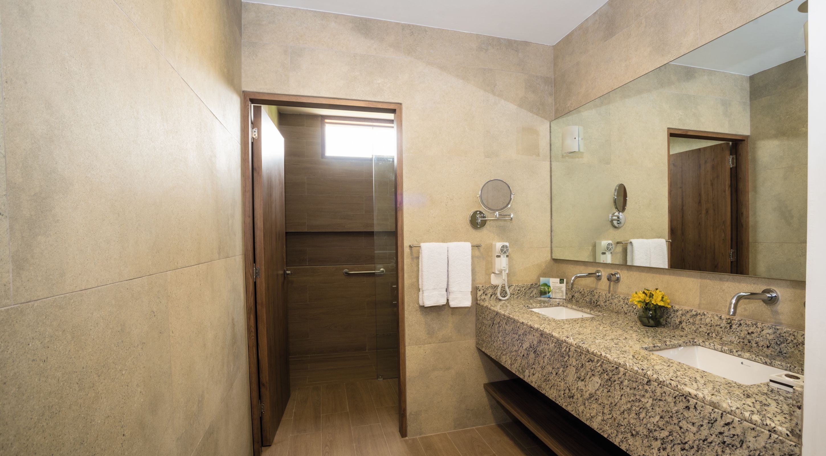 A modern bathroom with a granite countertop, a large mirror, and a shower area.
