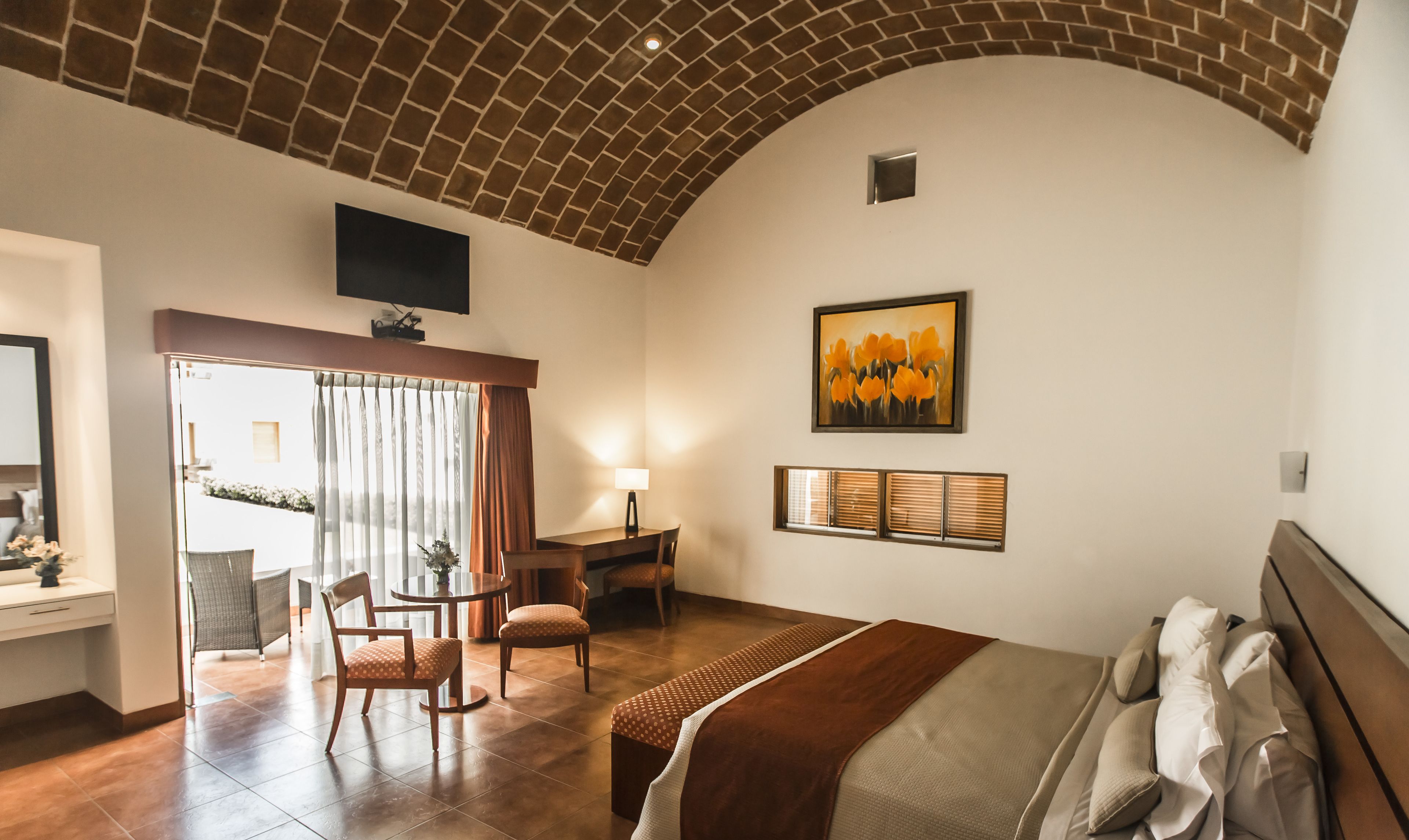 Habitación de hotel con techo de ladrillo, una cama, un escritorio con una silla, un televisor montado en la pared y un cuadro.