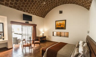 Habitación de hotel con techo de ladrillo, una cama, un escritorio con una silla, un televisor montado en la pared y un cuadro.