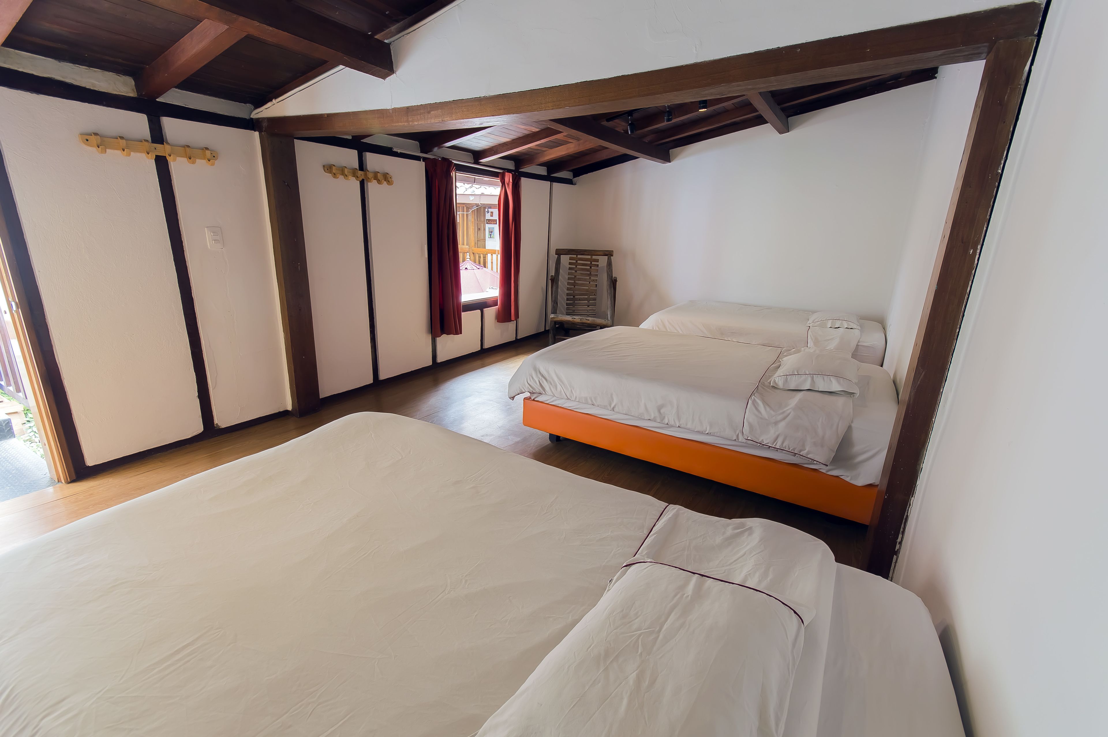 Una habitación con dos camas, vigas de madera, un puerta corredera y una ventana con cortinas.
