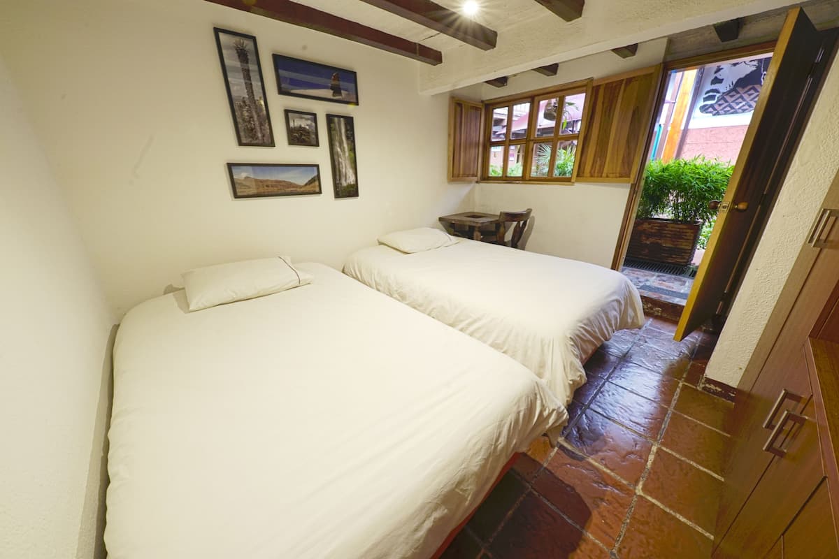 A room with two beds, a small table, and a window with wooden shutters.