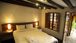 A neatly made bed with white linens and two towels, a wooden headboard, bedside lamps, a window with wooden shutters, and a door leading outside. - Masaya Bogotá (Bogotá)