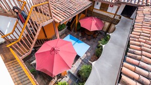 A courtyard with terracotta tiled roofs, wooden railings, and two red umbrellas providing shade. - Masaya Bogotá (Bogotá)