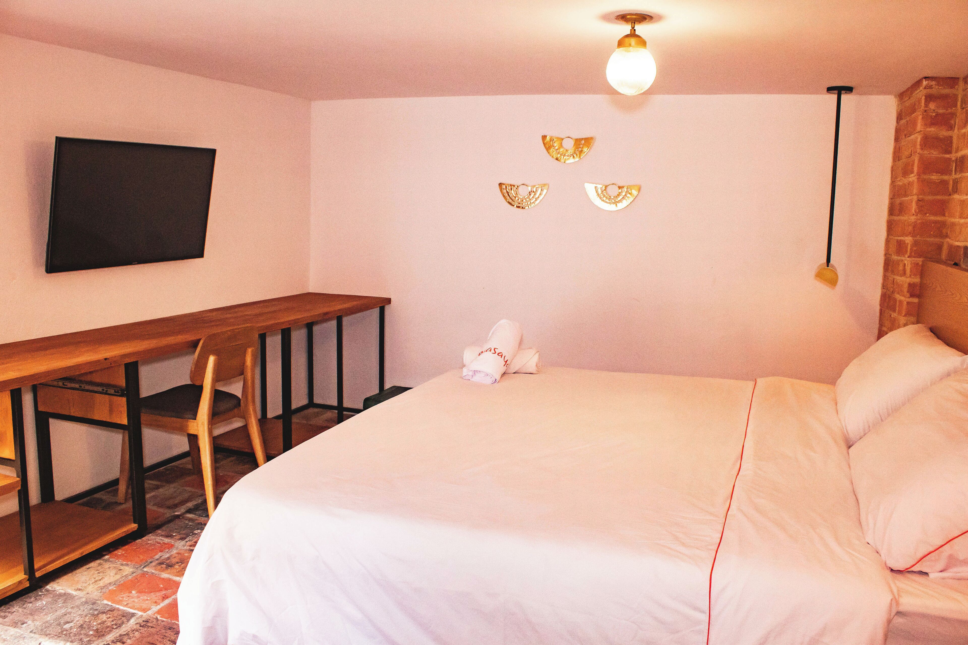 Ein Schlafzimmer mit einem Bett, einem Schreibtisch, einem Stuhl und einem an der Wand befestigten Fernseher.