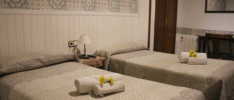 Habitación de hotel con dos camas, una mesita de noche, una lámpara y una pared con baldosas decorativas.