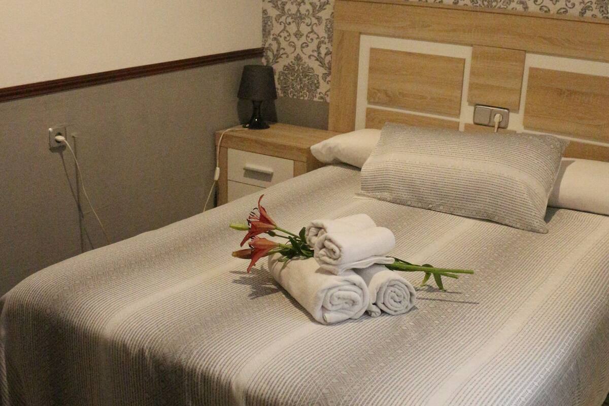 A neatly made bed with a striped bedspread, a pillow, and rolled towels. There is a framed picture on the wall above the bed.