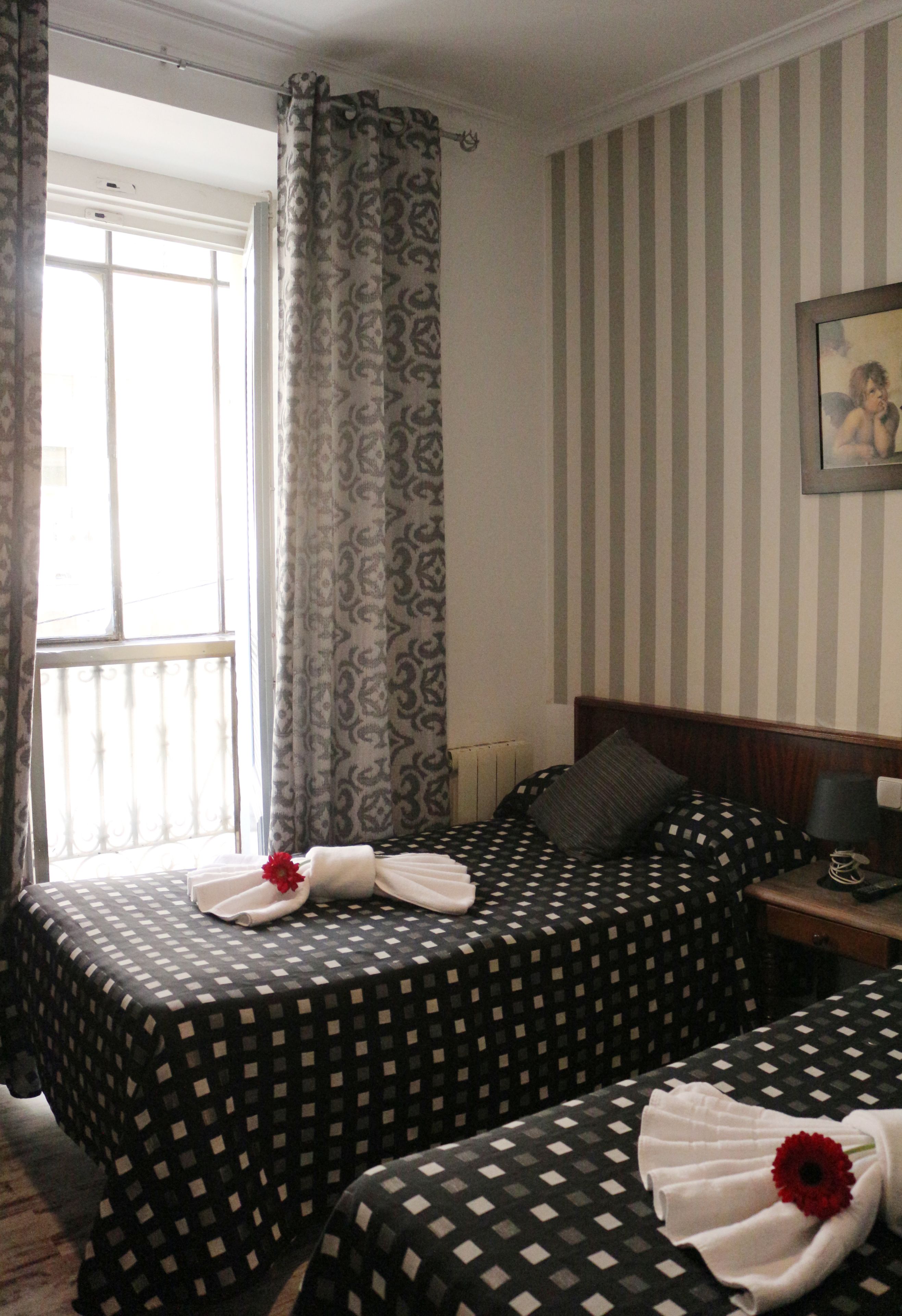 A hotel room with two beds, striped wallpaper, a framed picture on the wall, and a window with curtains.