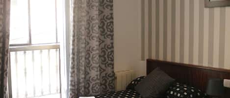 A hotel room with two beds, striped wallpaper, a framed picture on the wall, and a window with curtains.