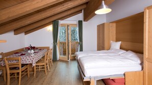 A cozy room with a wooden ceiling, a bed, a dining table with chairs, and a window with curtains. - Residence Civetta (Val di Zoldo)