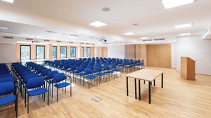 Un salón de conferencias con filas de sillas azules, una mesa de madera y un atril.