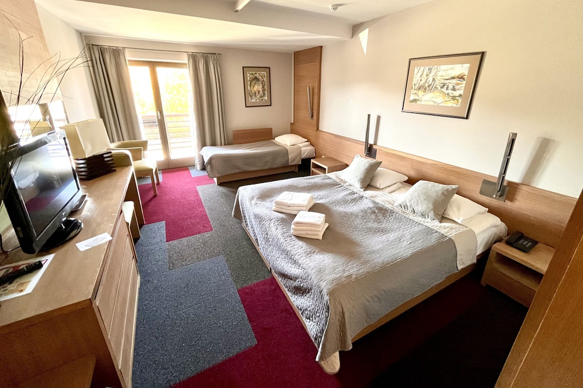 Habitación de hotel con dos camas, televisión, escritorio y ventana con cortinas.