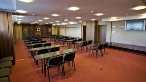 Un salón de conferencias con mesas y sillas, una pantalla de proyector y un televisor de pantalla plana.