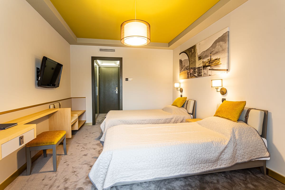 Habitación de hotel con dos camas, un escritorio, una silla, un televisor y un cuadro en la pared.